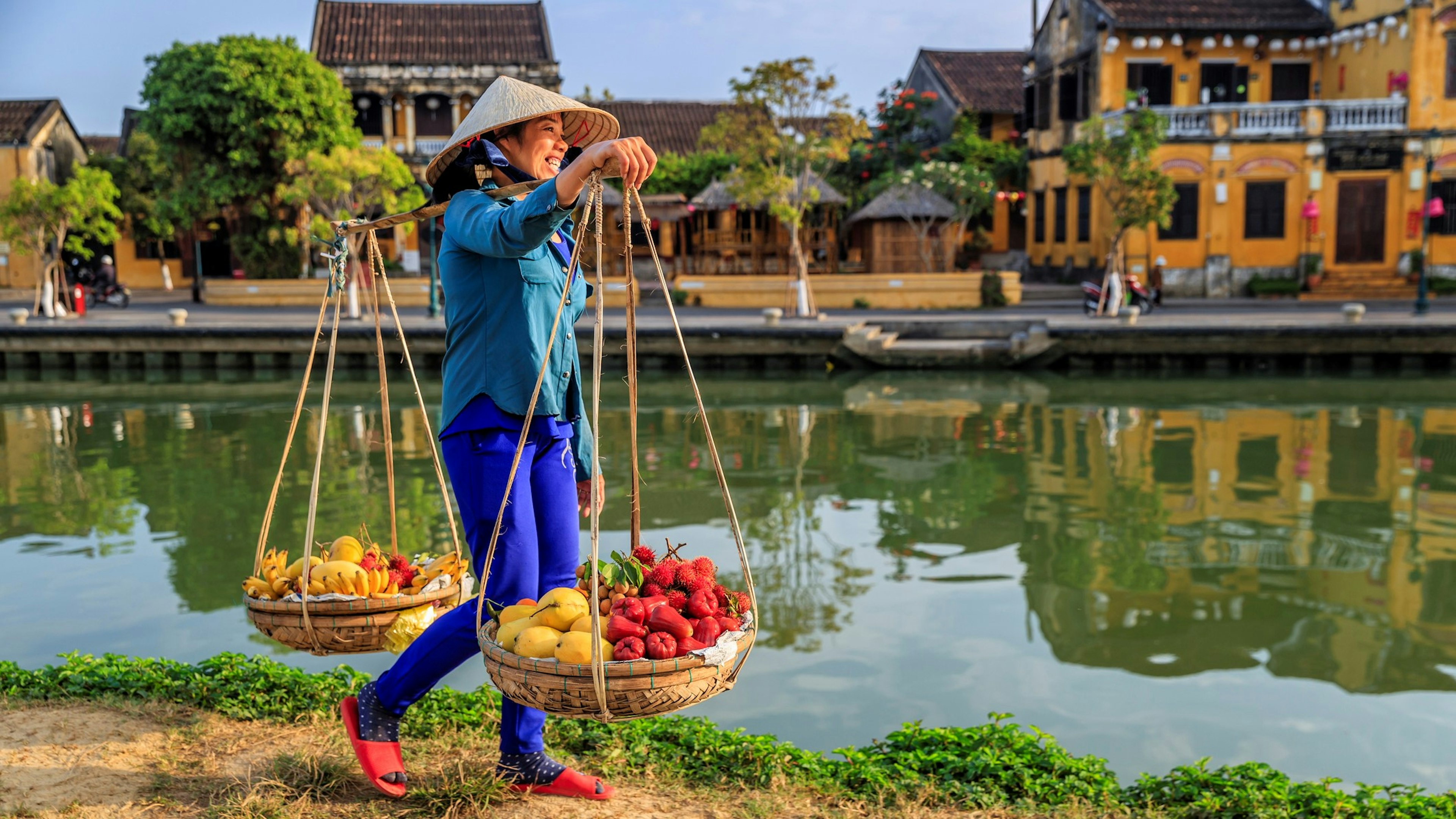 A woman carries baskets of fruit along a canal in the old town of Ha Noi, Vietnam