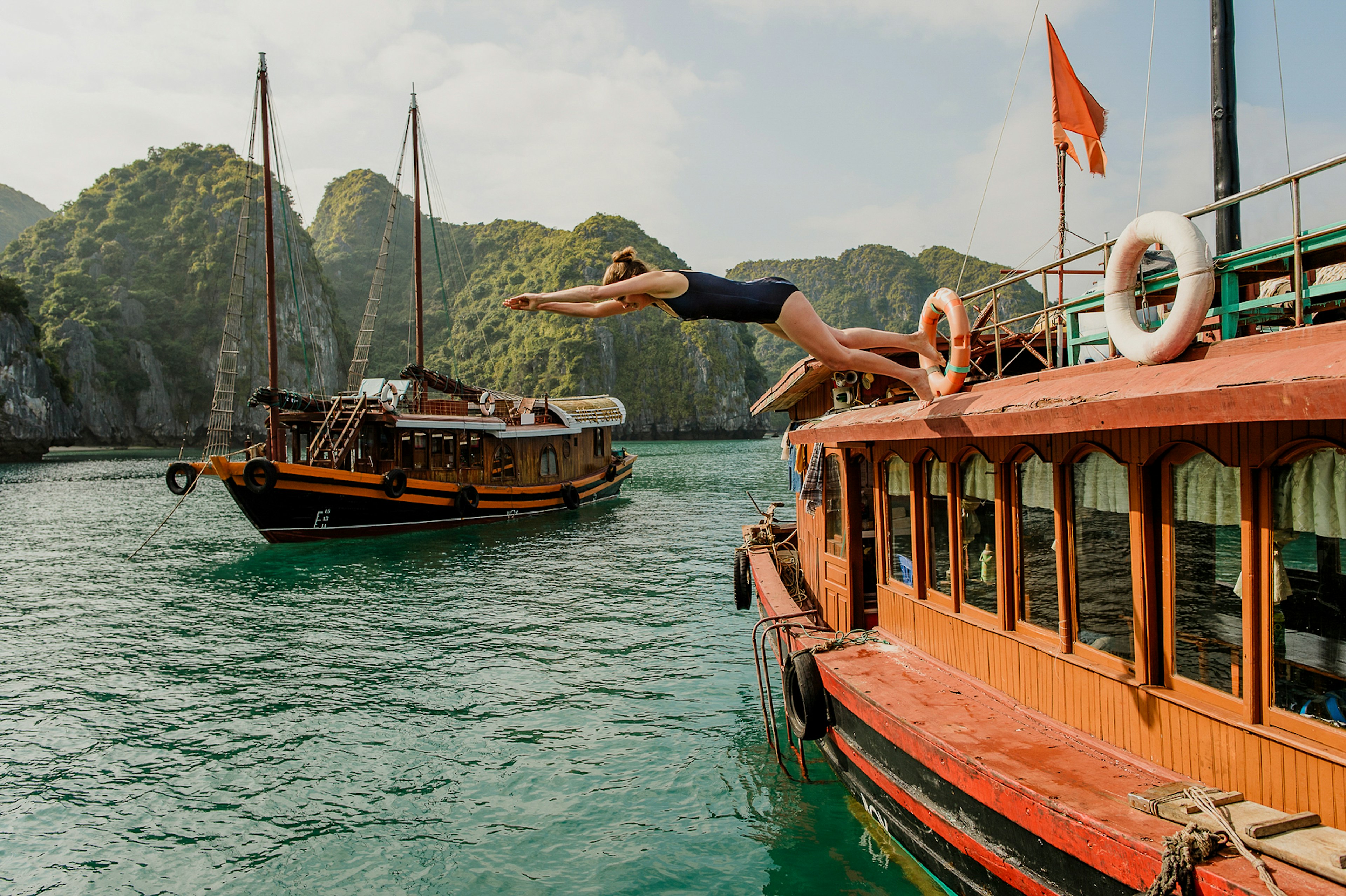 A woman dives from a boat into a bay with vast limestone outcrops