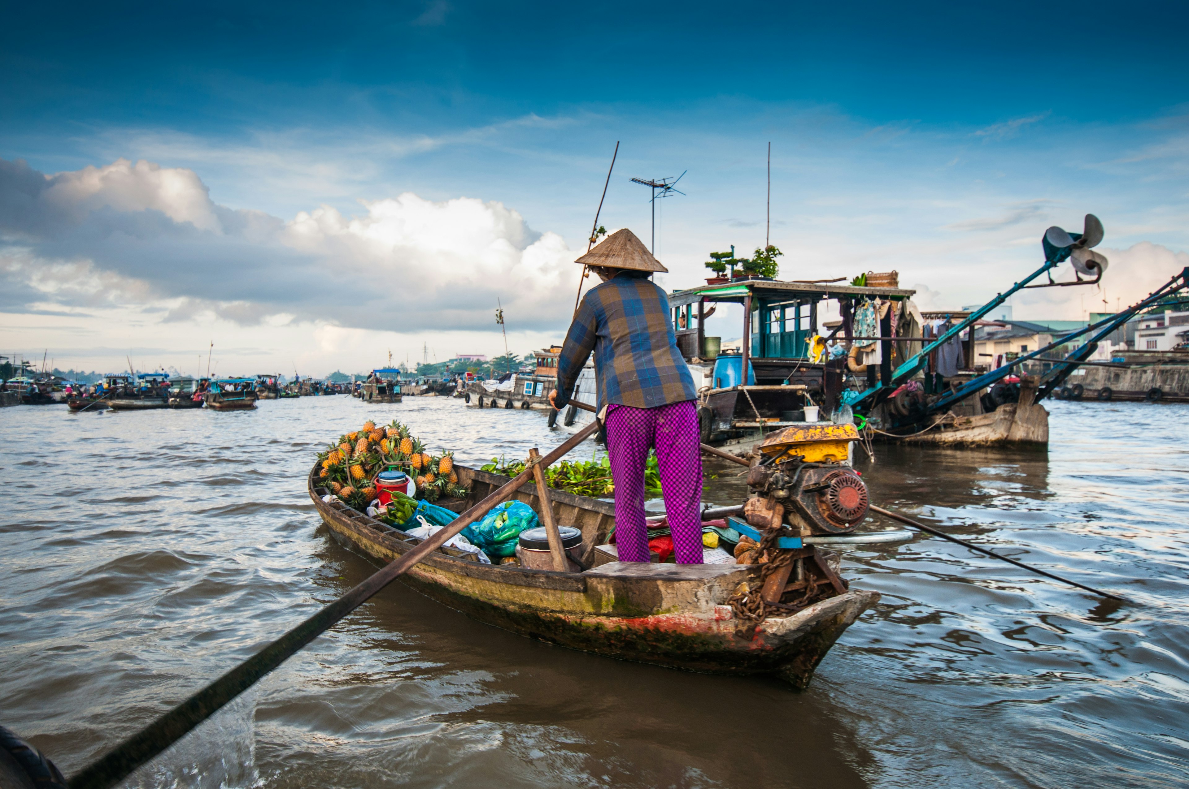 A woman in a conical hat pilots a small boat on a wide river