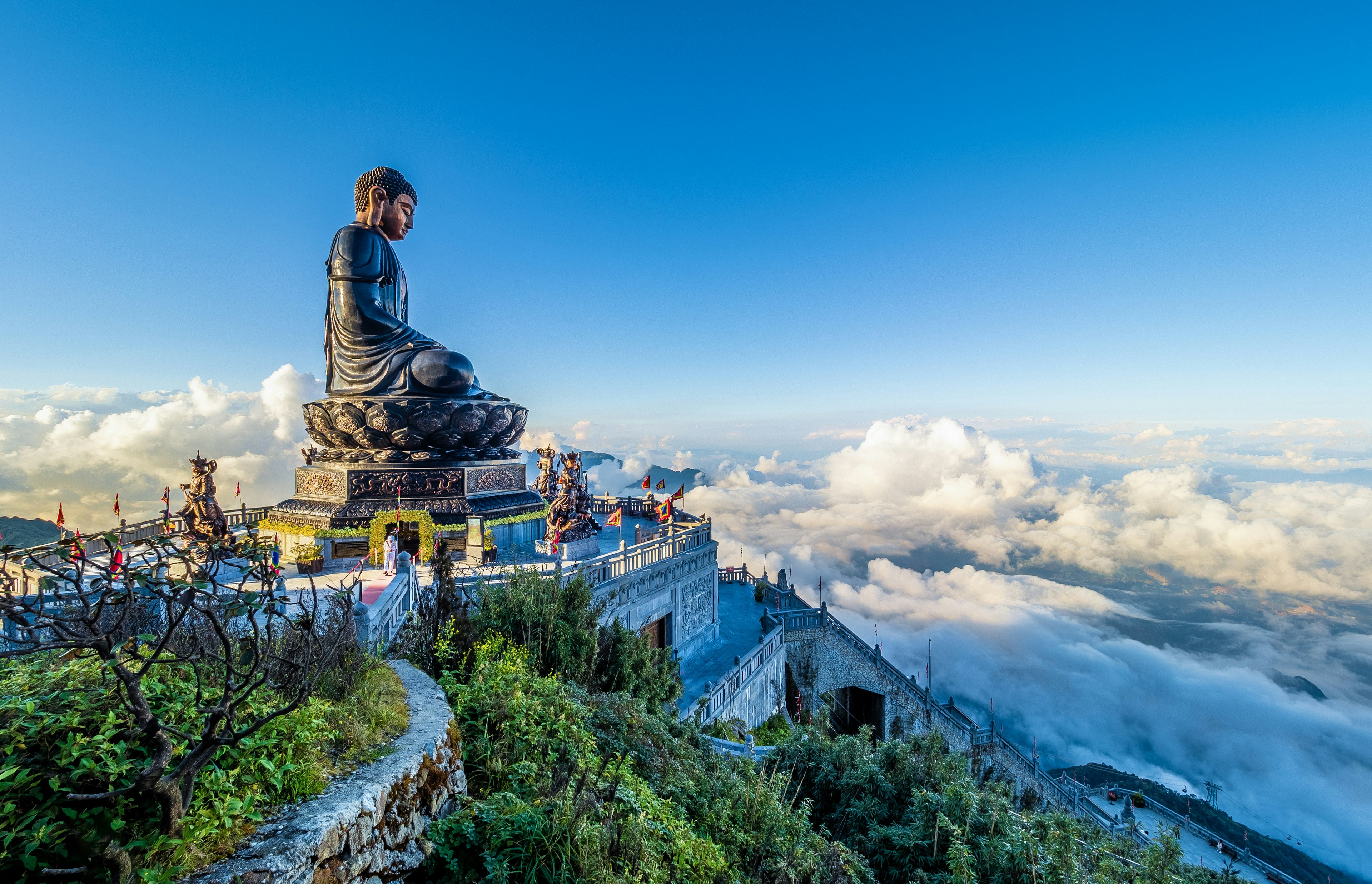 A giant Buddha statue and a terrace with views of the clouds and landscapes below from the top of Mount Fansipan, Đường District, Lai Chau, Vietnam