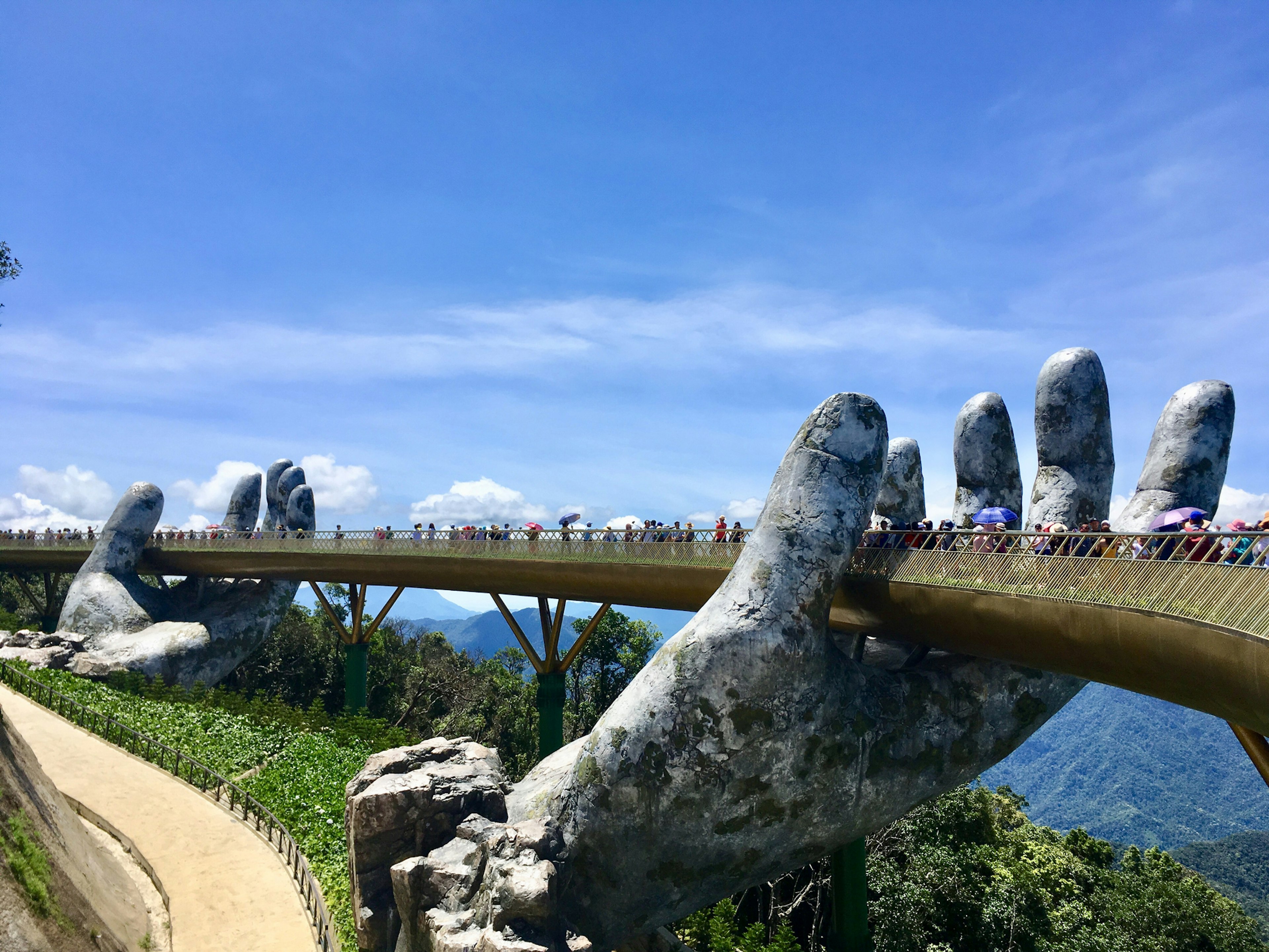 People walk along a bridge held by two giant stone hands in a mountain resort.